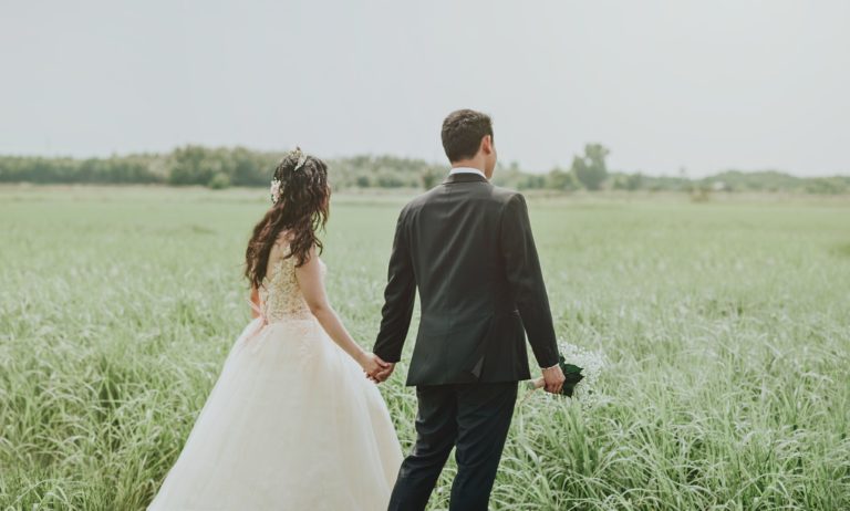 Husband and wife walking in a grass field.