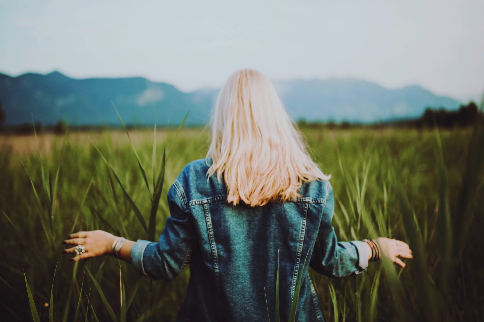 Blonde woman in tall grass field with hands lifted in prayer