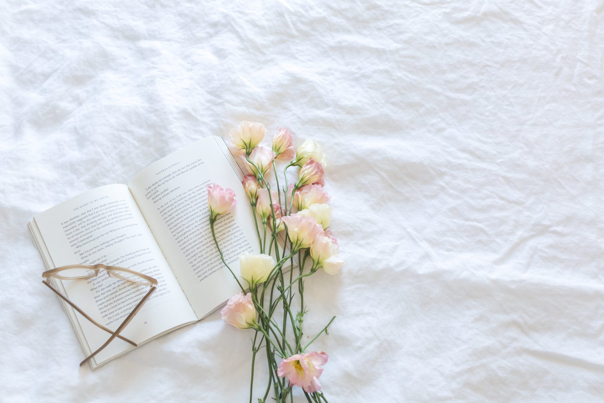 Christian book on white blanket with flowers and glasses